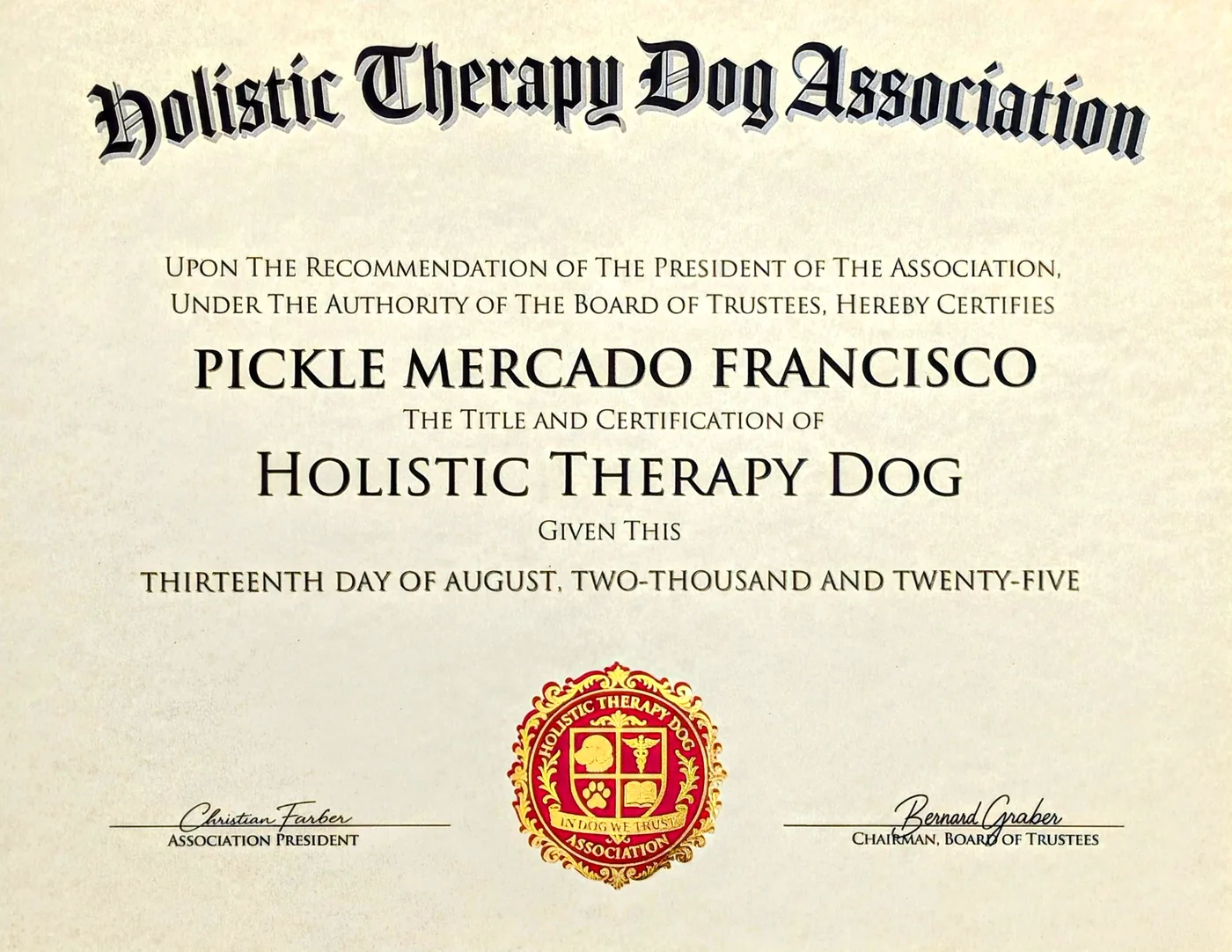 A printed diploma photographed flat, made out to Pickle
  Mercado Francisco: a blackletter wordmark, the title Holistic Therapy Dog,
  the granted date written out in words, a gold and red foil seal, and the
  signatures of the President and the Chairman of the Board.